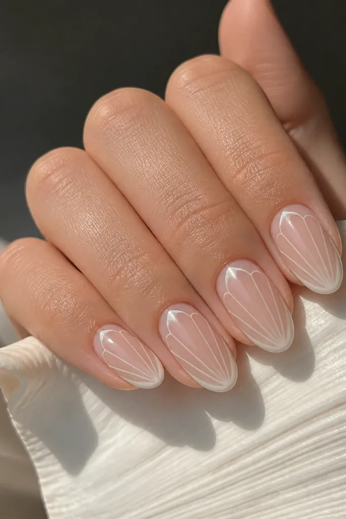 Neutral nude almond nails with negative space. The shell design is created by leaving thin clear gaps and outlining shell arcs in soft white-pearl, with the center mostly nude.