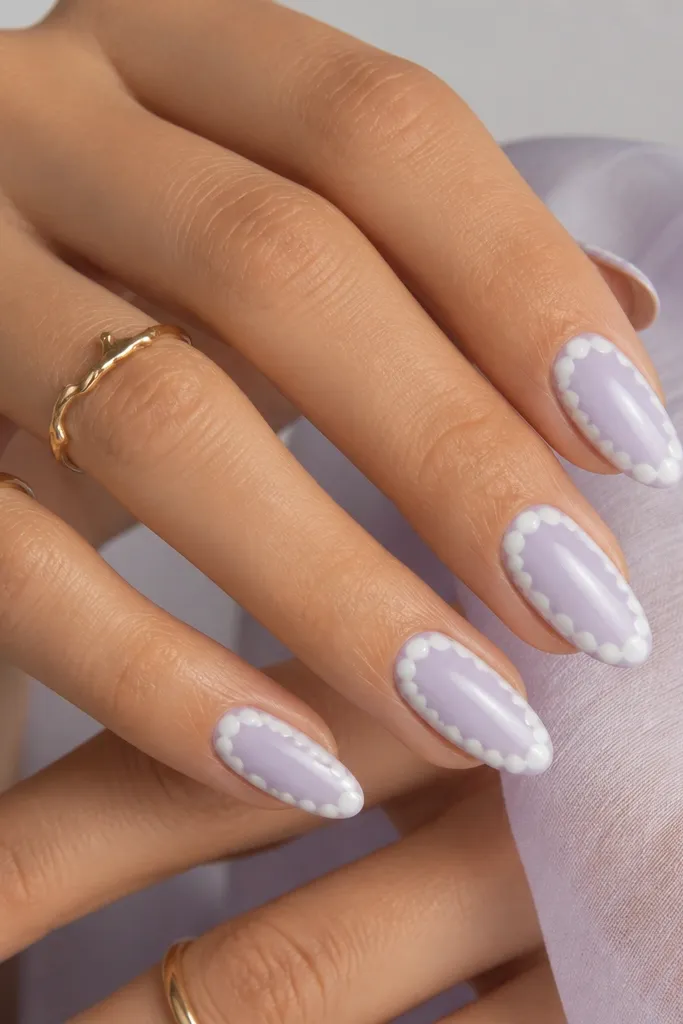 Milky lavender almond nails. Around the outer edge there is a scallop border made of small pearly white semicircles, with a soft lavender center and glossy finish.