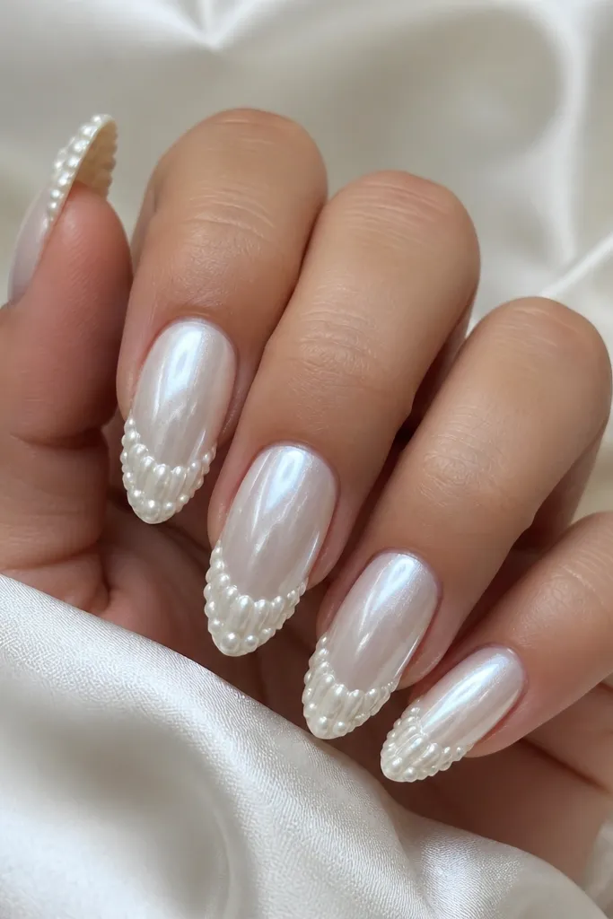 Pearl white almond nails with glossy gel. The tips have small 3D shell texture made from micro pearl beads, arranged in a scalloped ridge pattern along the outer edge.