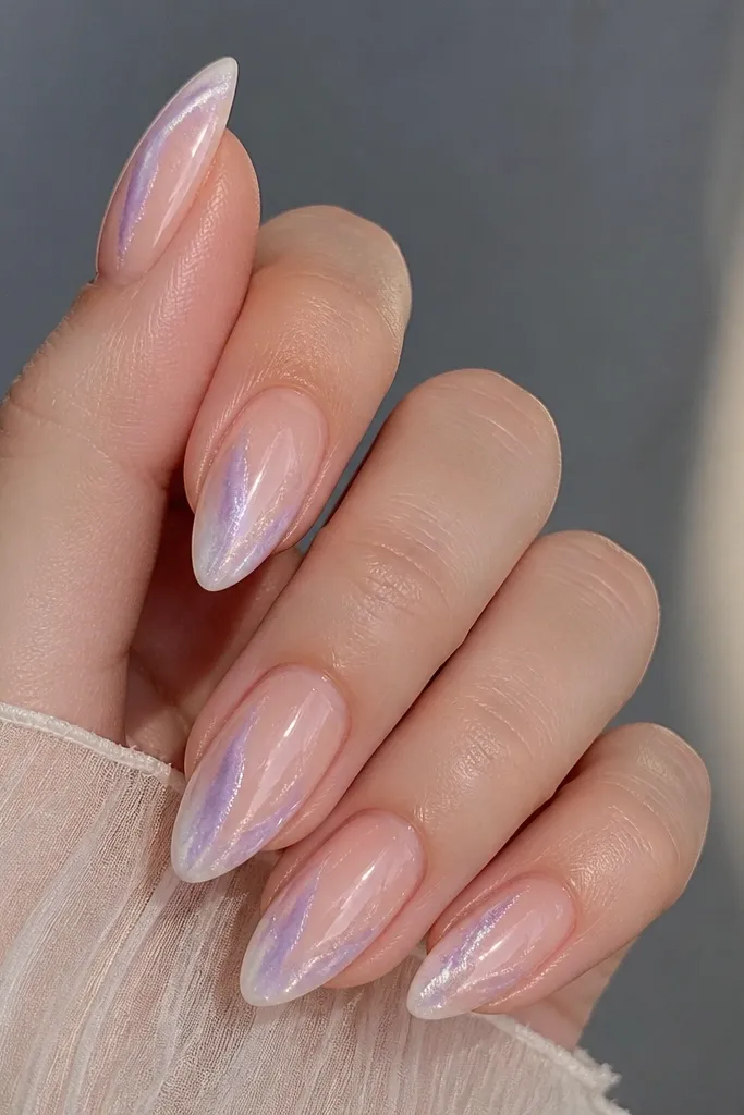 Soft nude almond nails with an ombré glow from the outer edge into the nail. Pearl-white and pale lilac create a galaxy-like shell fade, with subtle arc lines near the perimeter.