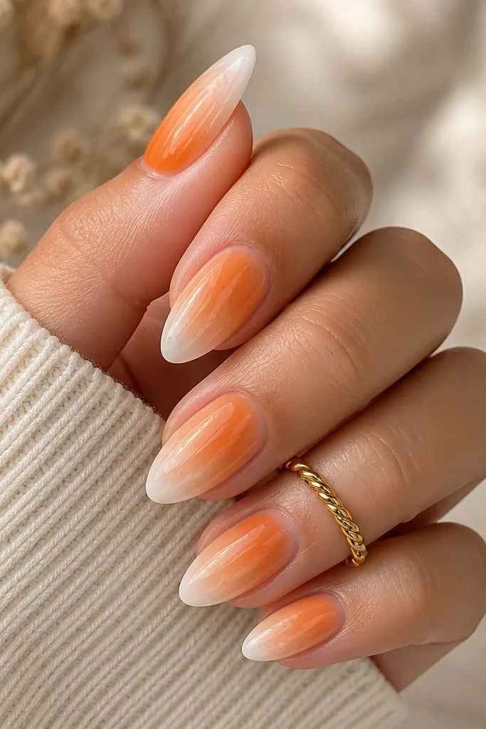 Almond nails with a smooth tangerine-to-sheer nude ombre; the top third has a soft white "cloud" fade near the tip; glossy finish.