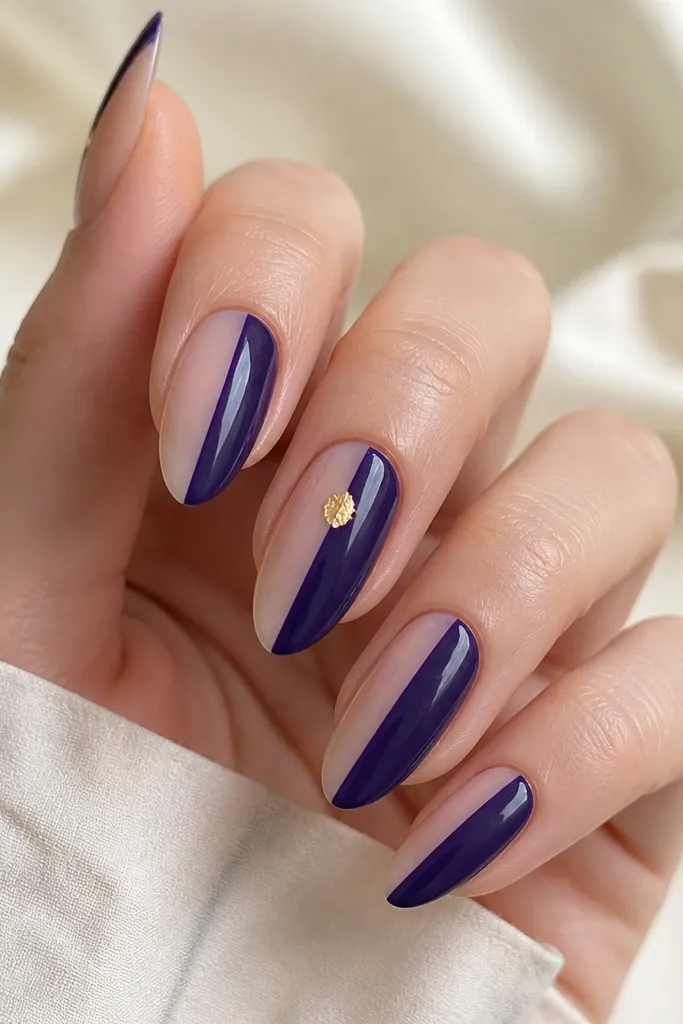 Almond nails split vertically: left side is sheer nude, right side is deep blueberry purple with a glossy finish; one nail has a tiny gold foil flake on the split line.