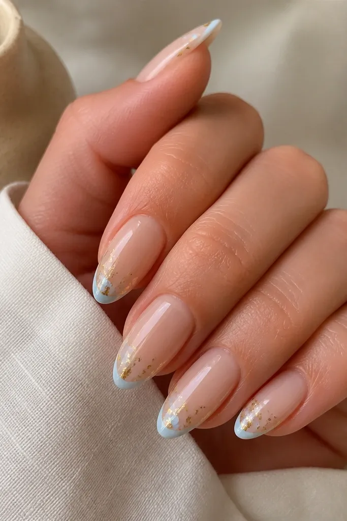 Almond nails with a sheer nude base, a very thin sky-blue French line at the tip, and scattered tiny gold foil specks around the line; glossy.
