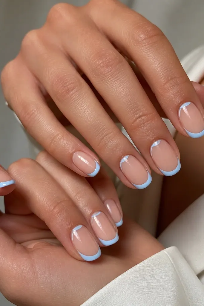 Nude base nails with baby blue French tips. On each nail, there is a smaller reverse half-moon accent near the side of the cuticle, outlined and filled lightly.