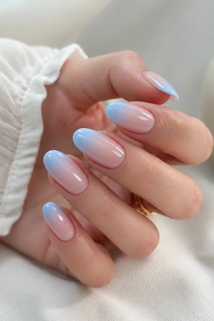 Nails with a nude base that gradually fades into baby blue at the tips. The French line is soft, with a smooth ombre transition and glossy finish.