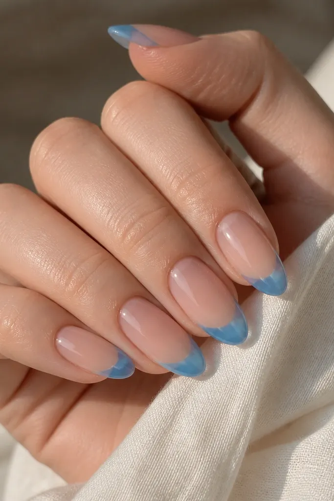 Nude base nails with baby blue French tips covered in a clear jelly layer. The tips look slightly translucent and glossy, like stained glass.