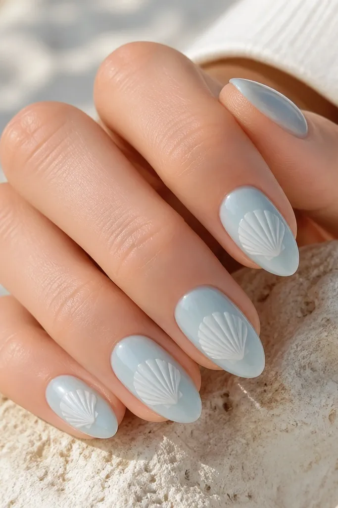 Medium almond nails in pale sea-glass blue with a milky sheen. Each nail has a single white shell shape centered, with delicate vein lines radiating outward like fan strokes.
