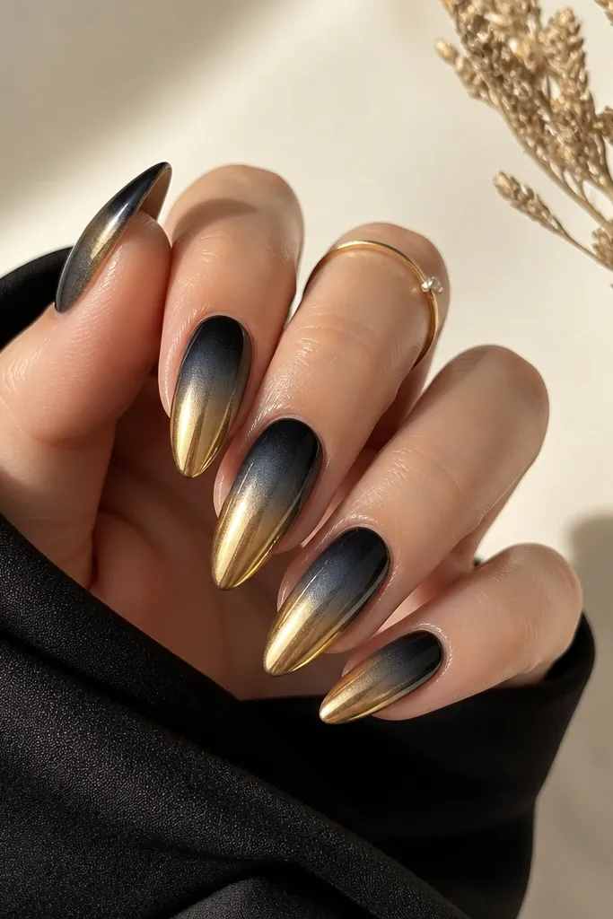 Almond nails with a soft black-to-gray smoke ombre from cuticle to mid-nail. The tips fade into a warm gold chrome that covers the last third of the nail in a smooth gradient.
