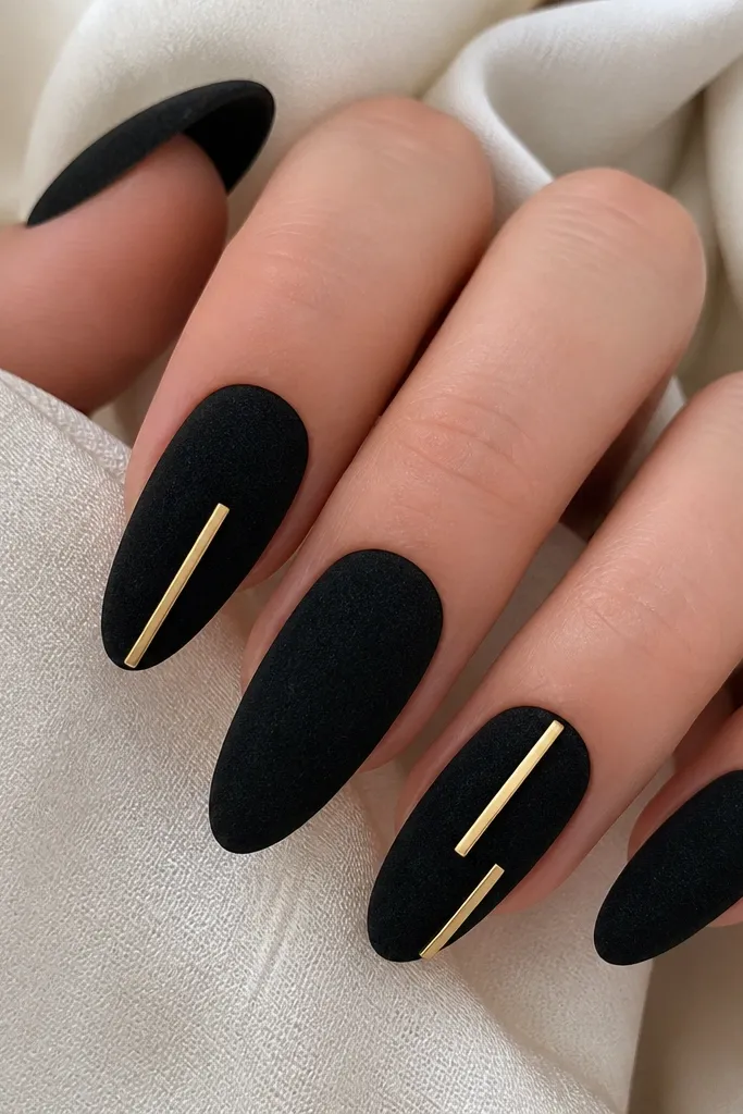 Almond nails with black velvet finish. Two nails have thin gold bar strips inlaid straight down the center and slightly offset, like metal bars. The bars have sharp edges and a satin shine.