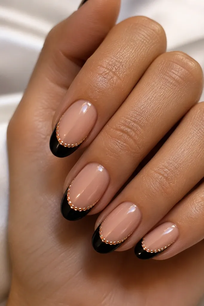 Black French tips on a nude base with a thin gold rhinestone "thread" running along the smile line. The stones are small and evenly spaced, catching light like jewelry.