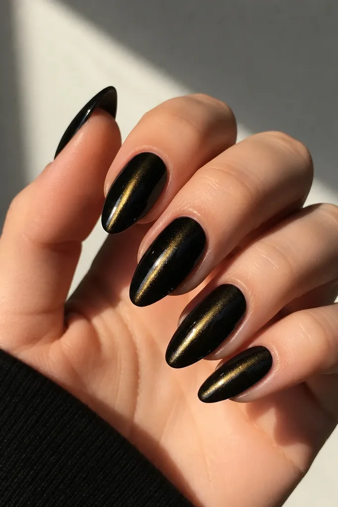 Medium almond nails with a deep black base, a gold cat-eye streak running down the center, and a high-gloss topcoat that makes the chrome line look like light.