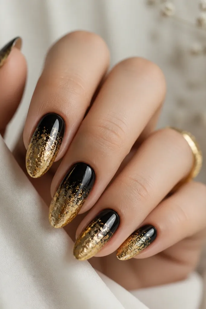 Medium almond nails with glossy black at the base fading into gold foil toward the tips, with a smooth transition and irregular foil texture.