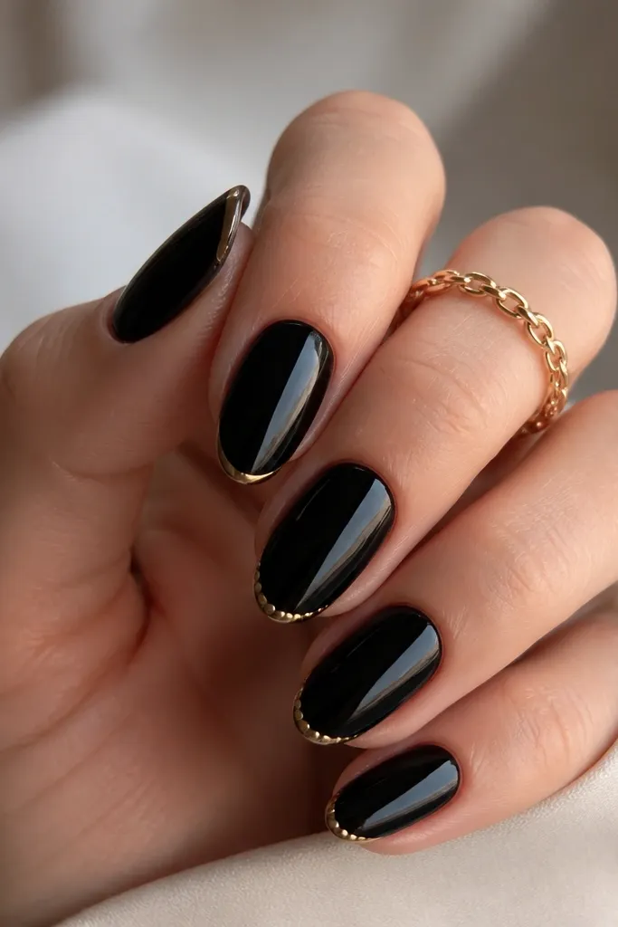 Medium oval nails with a glossy black base. A very thin gold French line sits at the tip edge. Between the gold line and the black, there are tiny gold micro dots spaced evenly on two accent nails.