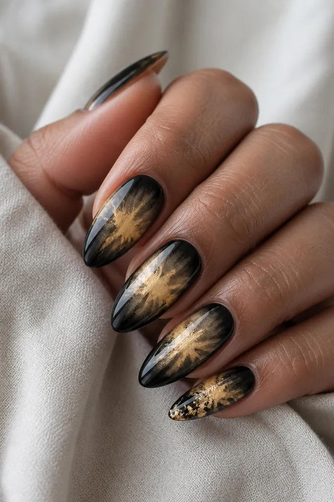Almond nails with glossy black. In the center of each nail, a soft gold leaf "aura" blooms outward like smoke, with the edges fading into black. One nail has extra leaf near the tip.