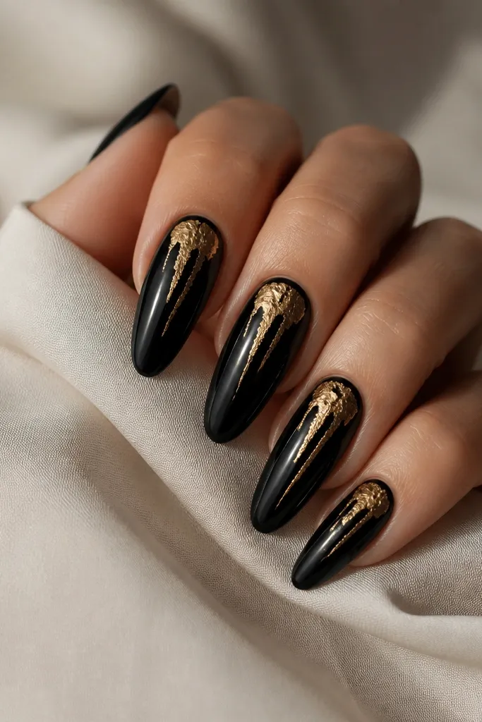 Long almond nails with glossy black. A gold leaf drip starts near the upper center and trails downward in two thin streaks, ending around mid-nail. The drip is irregular with black showing through.