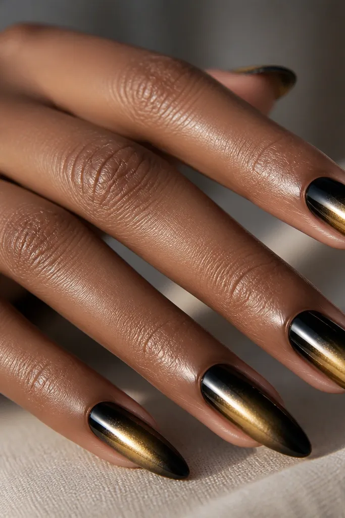 Nails with glossy black at the tips and a smooth fade into gold chrome near the center. The transition looks like a soft gradient, not a hard line.