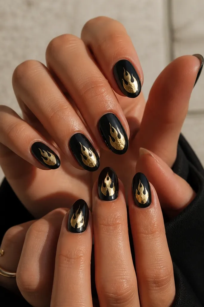 Black nails with gold foil shaped like small flames on the center of each nail. The foil edges look jagged and metallic, and everything is glossy.