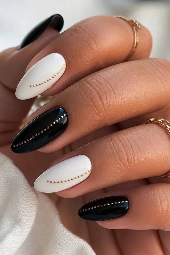 Long almond nails with a solid glossy black base and a single raised gold line near the cuticle made of tiny dot-like bumps, giving a beaded effect.