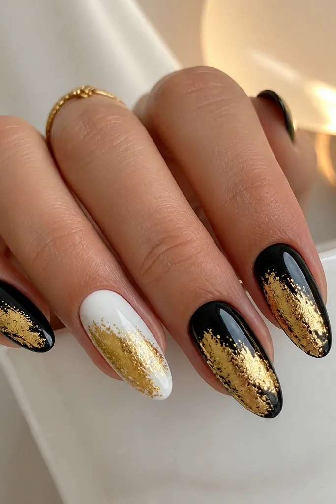Square nails painted glossy black with a horizontal gold foil smudge across the center, irregular and smoky, like a band of melted foil; the rest of the nail remains black.
