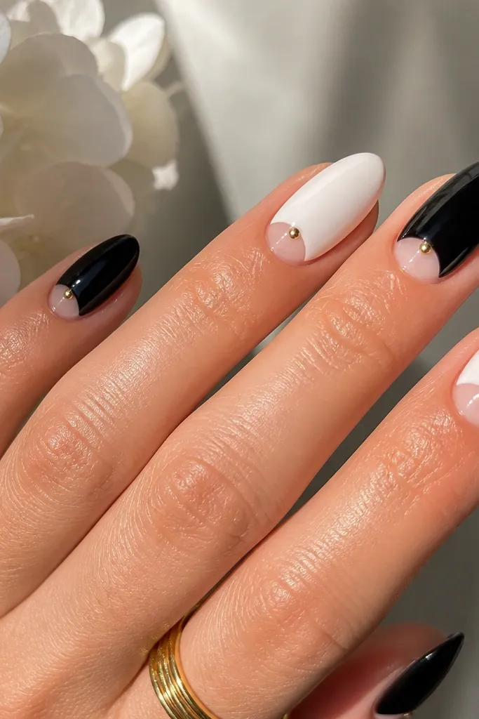 Short nails with a glossy black base only on the outer sides, leaving a clear negative space half-moon near the cuticle; scattered tiny gold dots sit across the black areas.