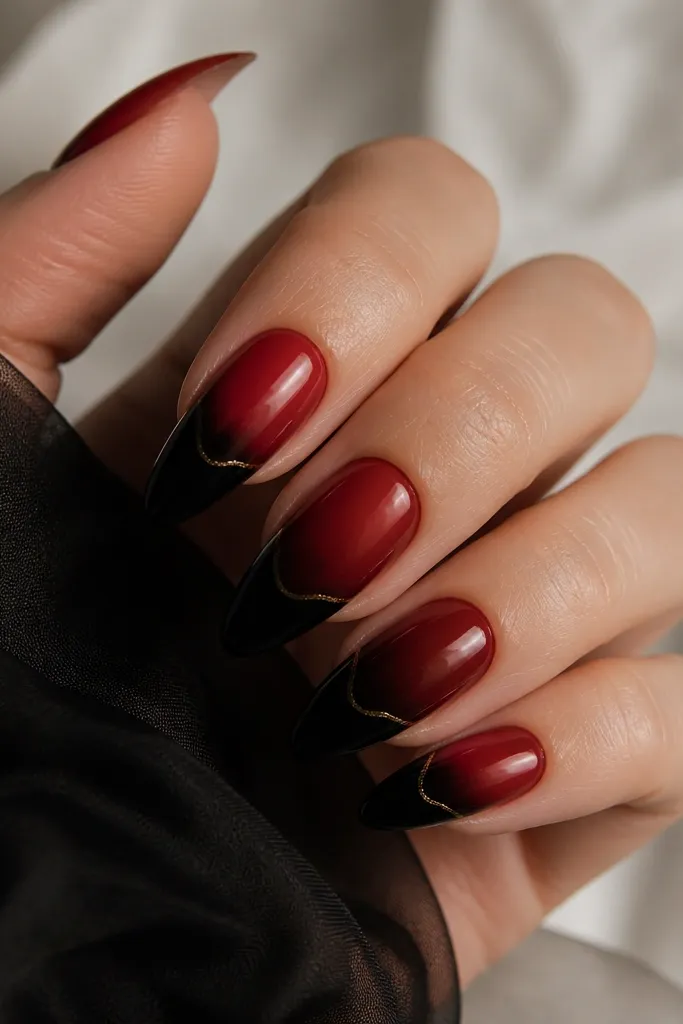 Long almond nails with a smooth ombre from deep red at the cuticle fading into black at the tip, finished with a thin gold outline following the ombre boundary.