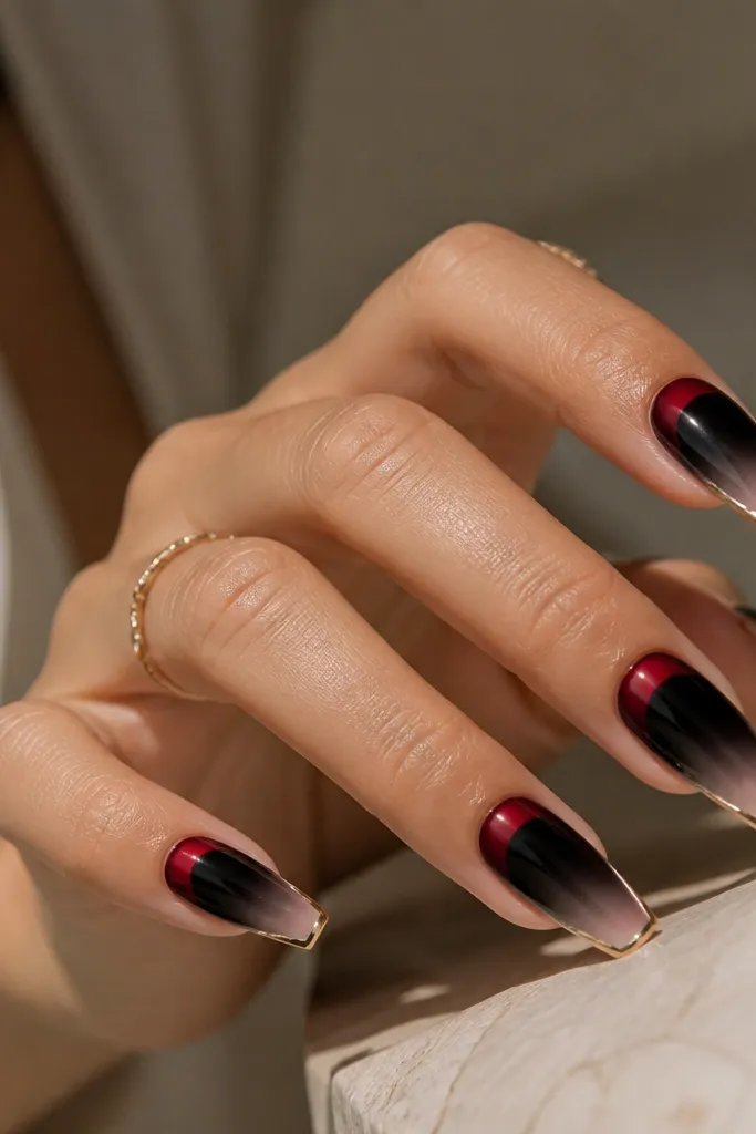 Short coffin nails fading from black at the cuticle into a softer black-to-clear gradient, with a red "glow" near the top edge and a thin gold line at the free edge.