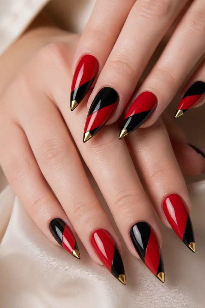 Stiletto nails with alternating red and black diagonal stripes, and a small gold corner accent at the tip on each nail.
