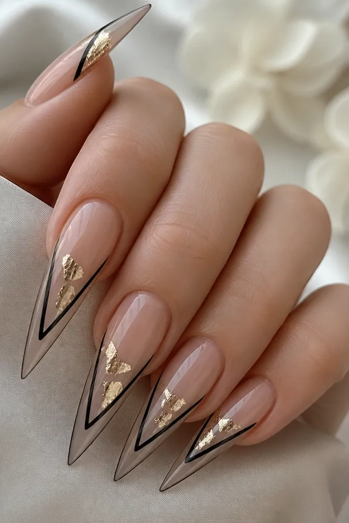 Stiletto nails with clear or nude base and black lines forming a partial outline; gold leaf pieces sit along the negative space near the center and tip, with crisp edges.