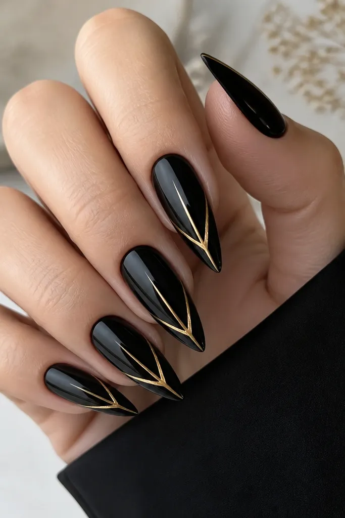 Black glossy stiletto nails with a centered gold chevron line running from near the cuticle down to the tip; the chevron is sharp and symmetrical.