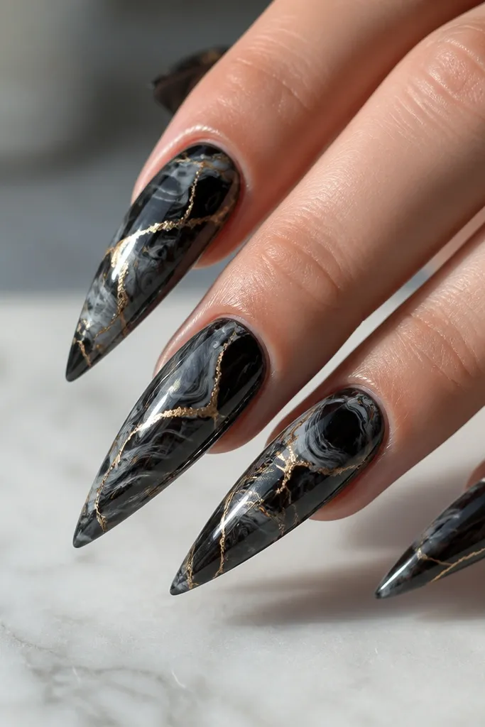 Stiletto nails with black marble swirls on a glossy base; thin gold veins run through the marble like natural stone.