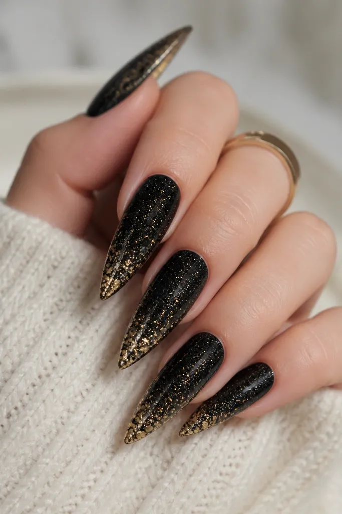 Stiletto nails with black glitter gel across the nail; the free edge has a concentrated line of gold flakes that fade inward slightly.