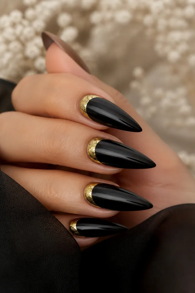 Stiletto nails with black base; a gold foil reverse French sits near the cuticle, forming a curved band that mirrors the French tip.