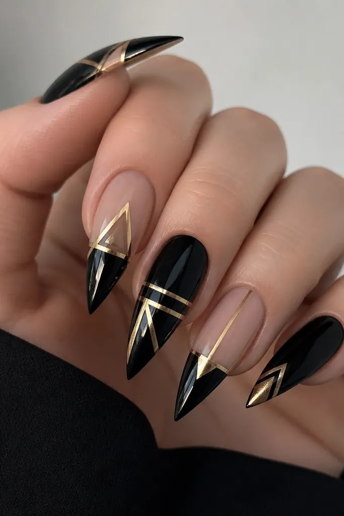 Stiletto nails with glossy black background and gold geometric shapes made from clean triangles and bars; some panels are negative space in nude.