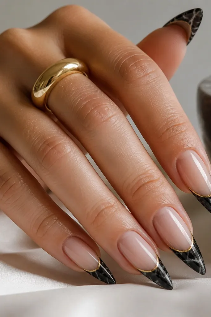 Stiletto nails with a marble effect on the tips like black stone; the cuticle area is sheer nude; gold micro lines sit at the very tip edge.