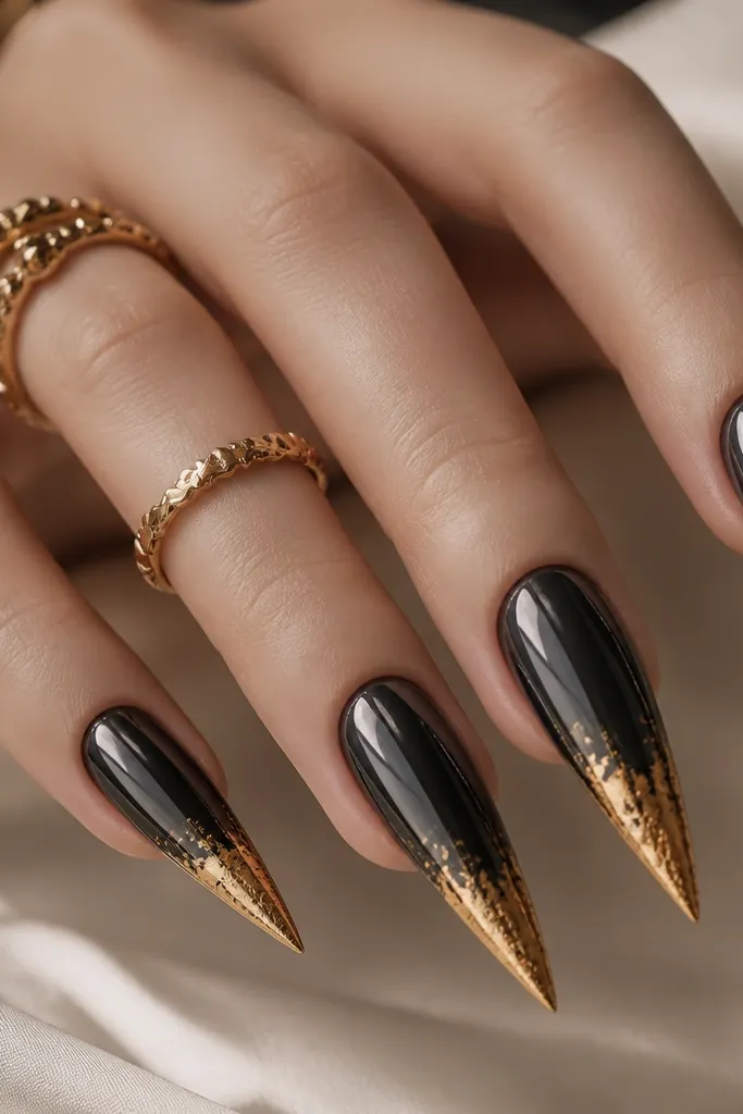 Stiletto nails with deep black chrome that reflects like metal; gold foil is concentrated at the tip edge and fades upward in a soft gradient.