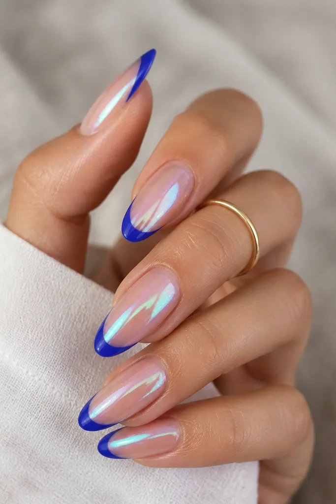 Medium almond nails with royal blue French tips. The chrome finish has a slight holographic shift - you see hints of teal and pink in the reflection. The base is sheer nude and the tips have a crisp curve.