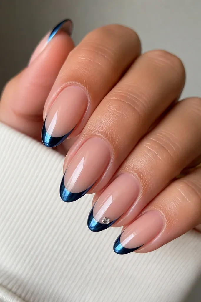 Medium almond nails with a classic blue chrome French tip. One nail has a tiny clear crystal placed at the outer corner of the smile line. The base is sheer nude and everything is glossy.