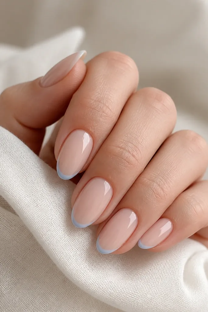 Close-up of almond nails with a very thin cornflower-blue French line centered at the free edge; nude pink base, glossy finish, clean curved smile line on all nails.