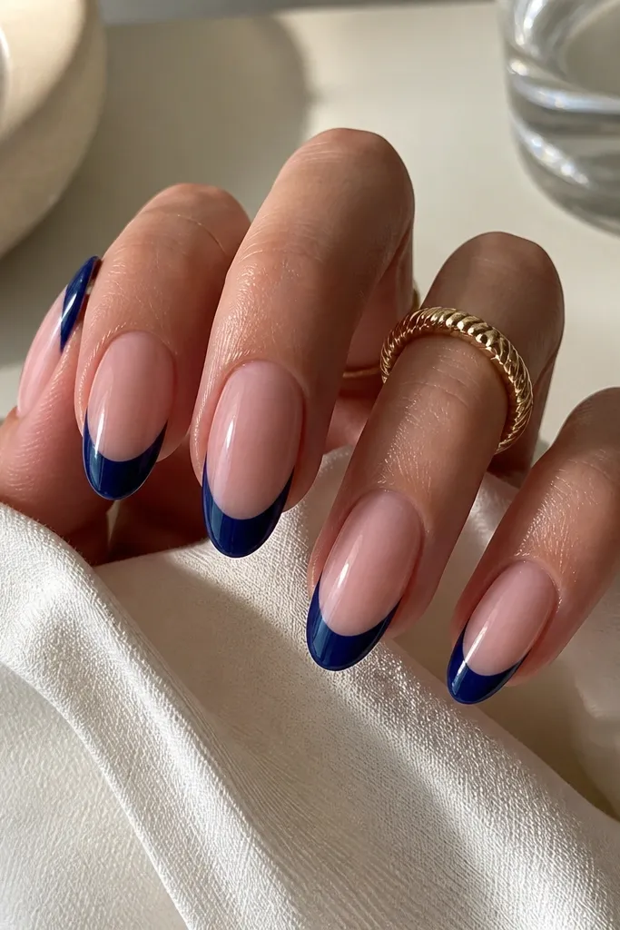 Almond nails in a nude base with a bold denim navy French tip that reaches the sides evenly; the French curve is crisp and glossy, no extra art.