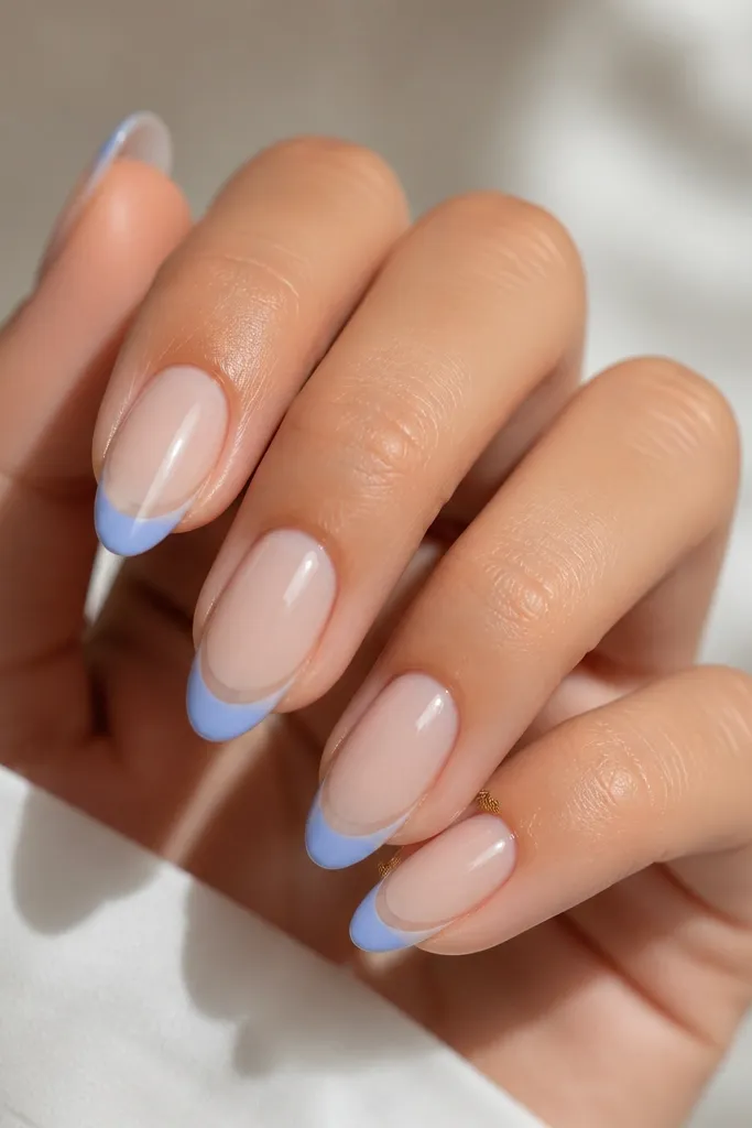 Almond nails with a sheer nude base; a narrow icy periwinkle French tip with a clear gap between the tip and the base, glossy topcoat.
