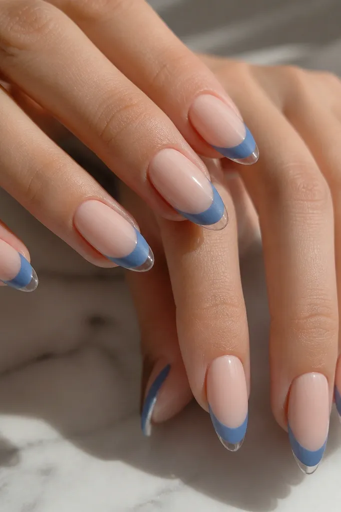 Almond nails with a nude base; blue French tips are matte, while the very tip edge has a glossy clear cap; the line between matte and gloss is visible.