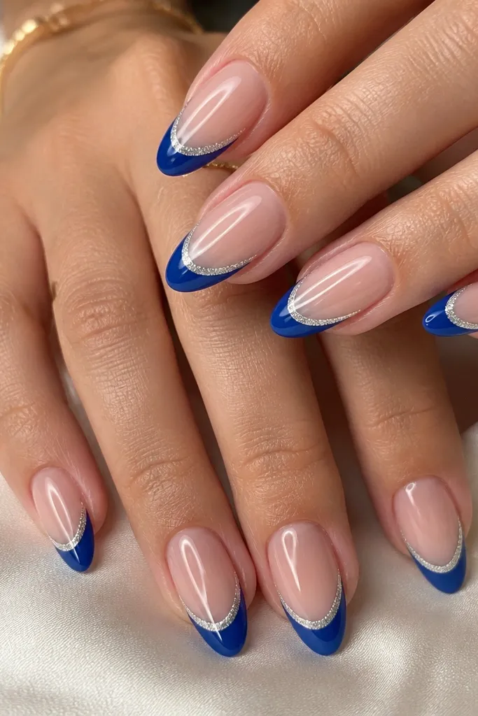 Almond nails with nude base; royal blue French tips with a thin silver line running parallel inside the smile curve; glossy finish.