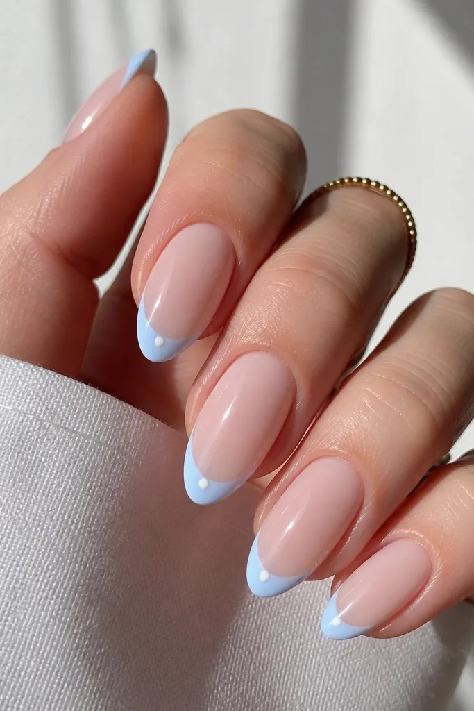 Almond nails with nude base; baby blue French tips and a single tiny white dot at the center of each blue tip; glossy finish.