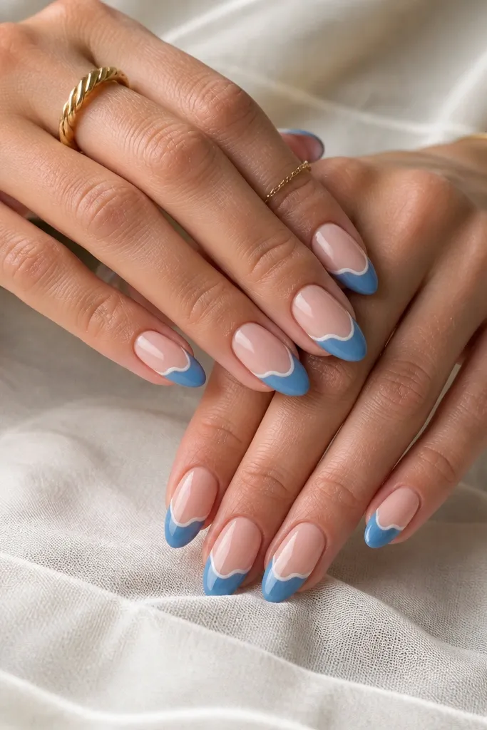 Almond nails with nude base; ocean blue French tips with a thin white wavy line along the inner edge; glossy finish.