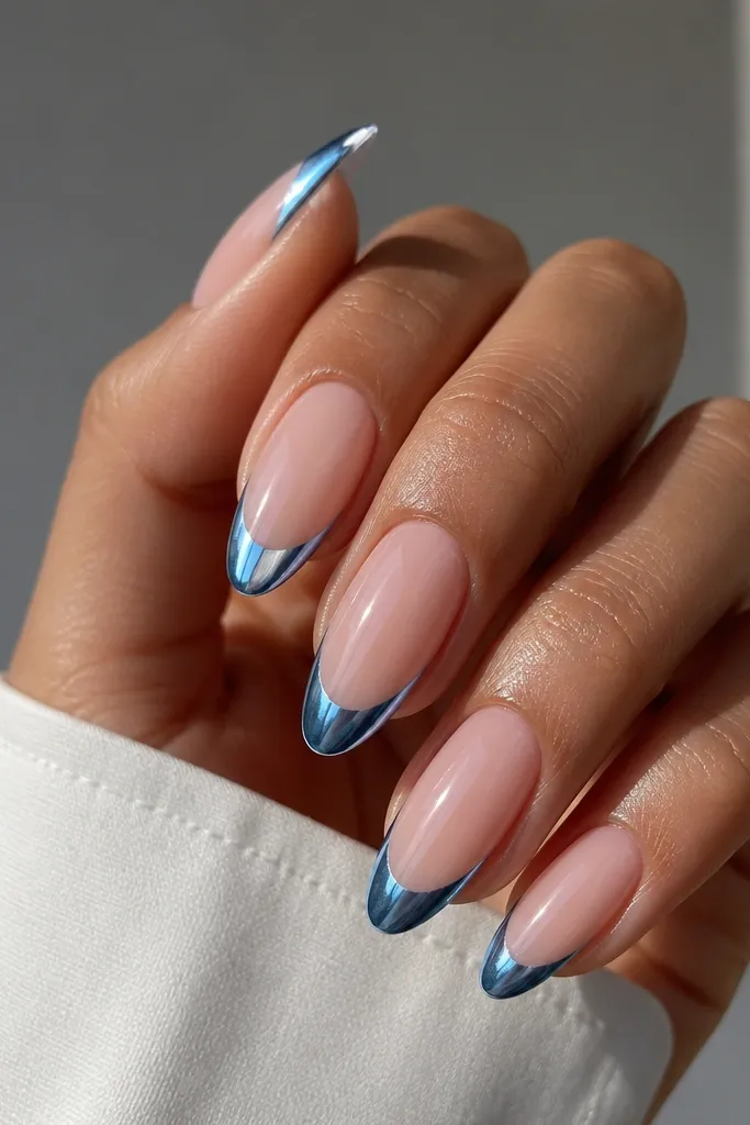 Almond nails with nude base; blue chrome French tips that reflect light like metal; glossy topcoat for mirror shine.