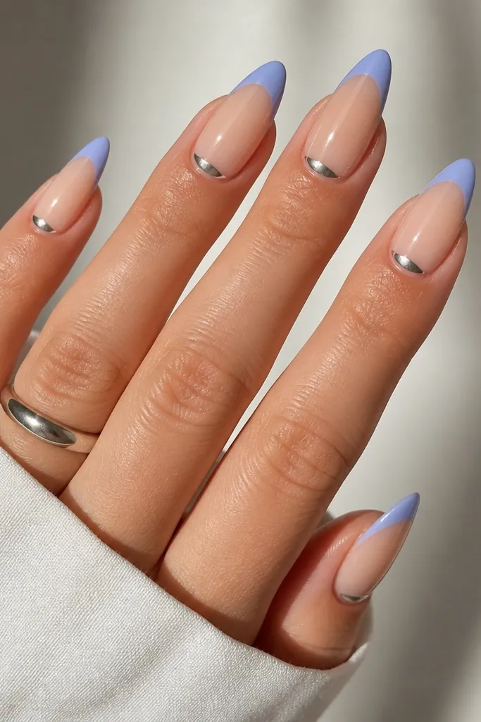 Almond nails with sheer nude base; periwinkle French tips; tiny silver half-moons at the cuticle on each nail; glossy finish.