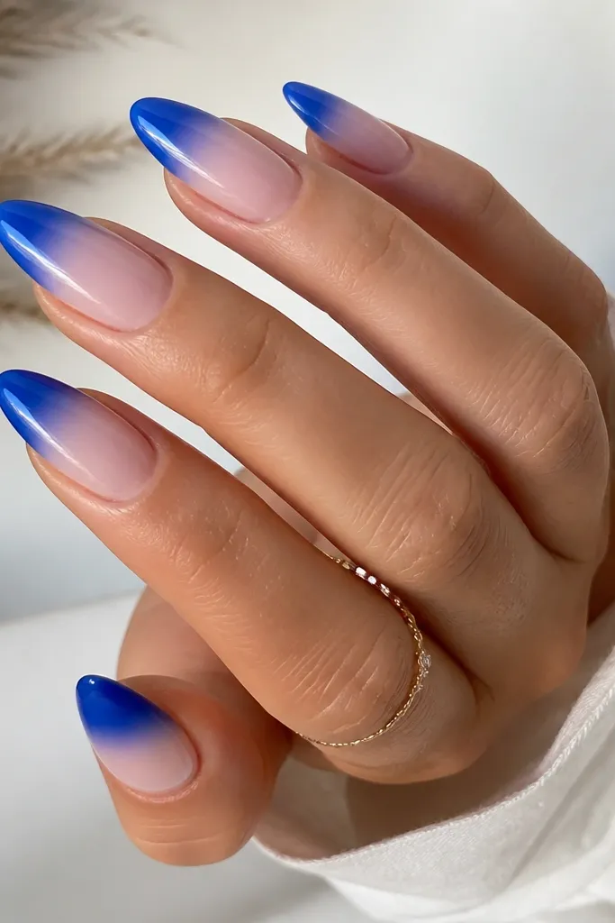 Almond nails with nude base; royal blue ombre that starts at the French free edge and fades smoothly into nude; glossy finish.