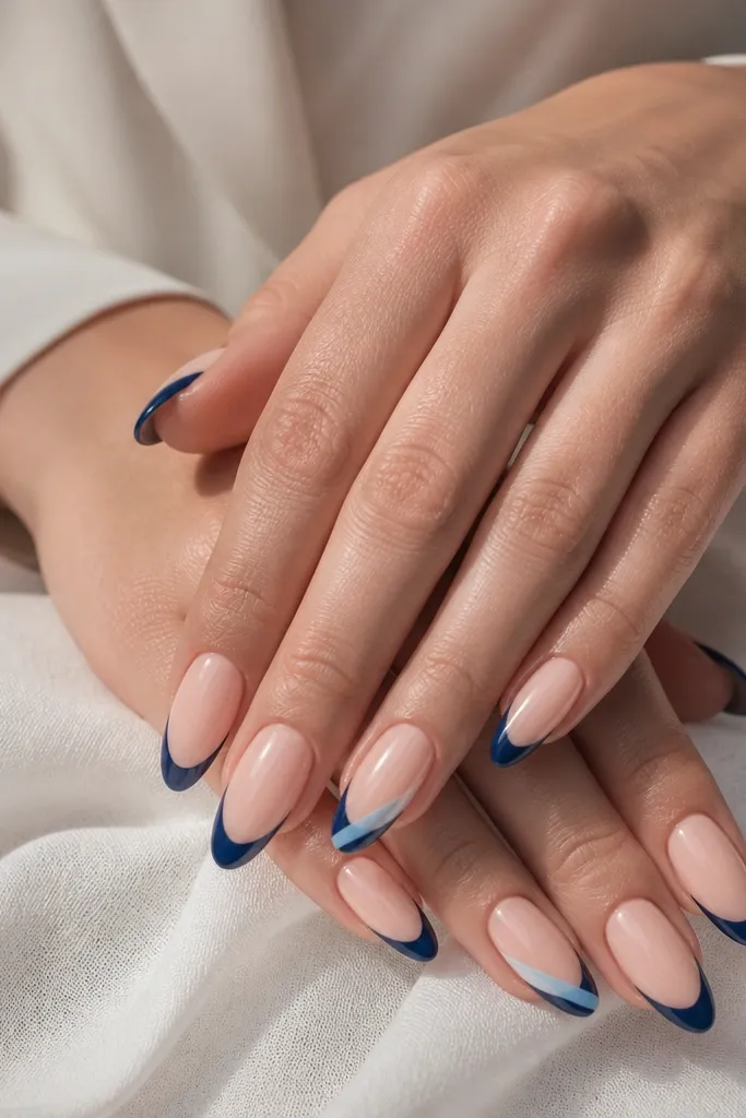 Almond nails with nude base; navy French tips; on ring fingers a light blue diagonal slash crosses the French area; glossy finish.