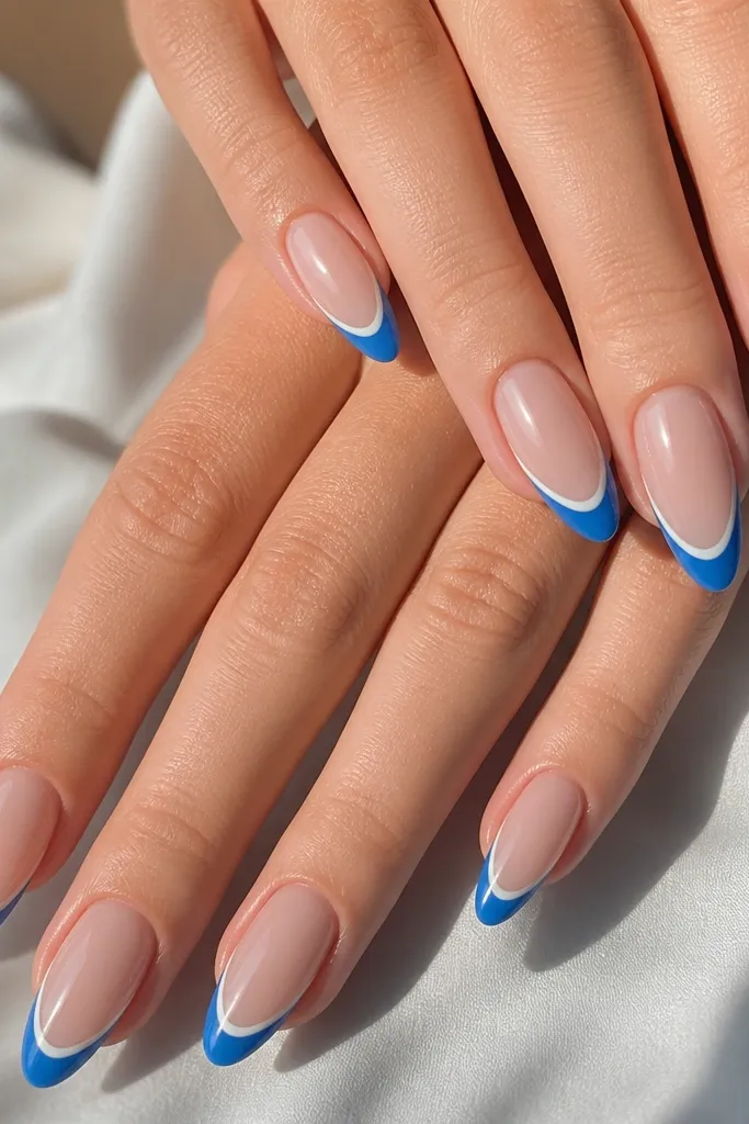 Almond nails with nude base; bright blue French tips outlined with a thin white border just inside the blue; glossy finish.