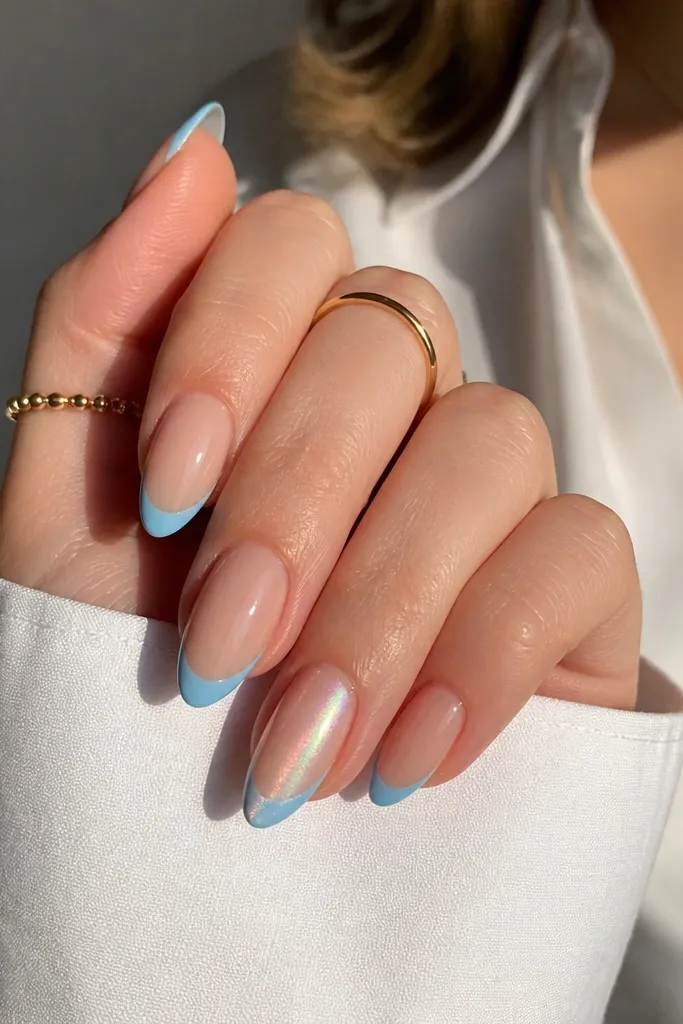 Almond nails with nude base and classic blue French tips; one accent nail has aurora chrome shimmer over the blue tip while others stay plain; glossy finish.